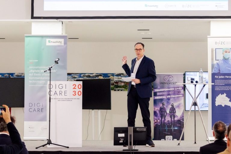 Marcel Weigand moderiert die zweitägige DigiCare 2030 Veranstaltung Marcel Weigand steht auf einer Bühne und moderiert.